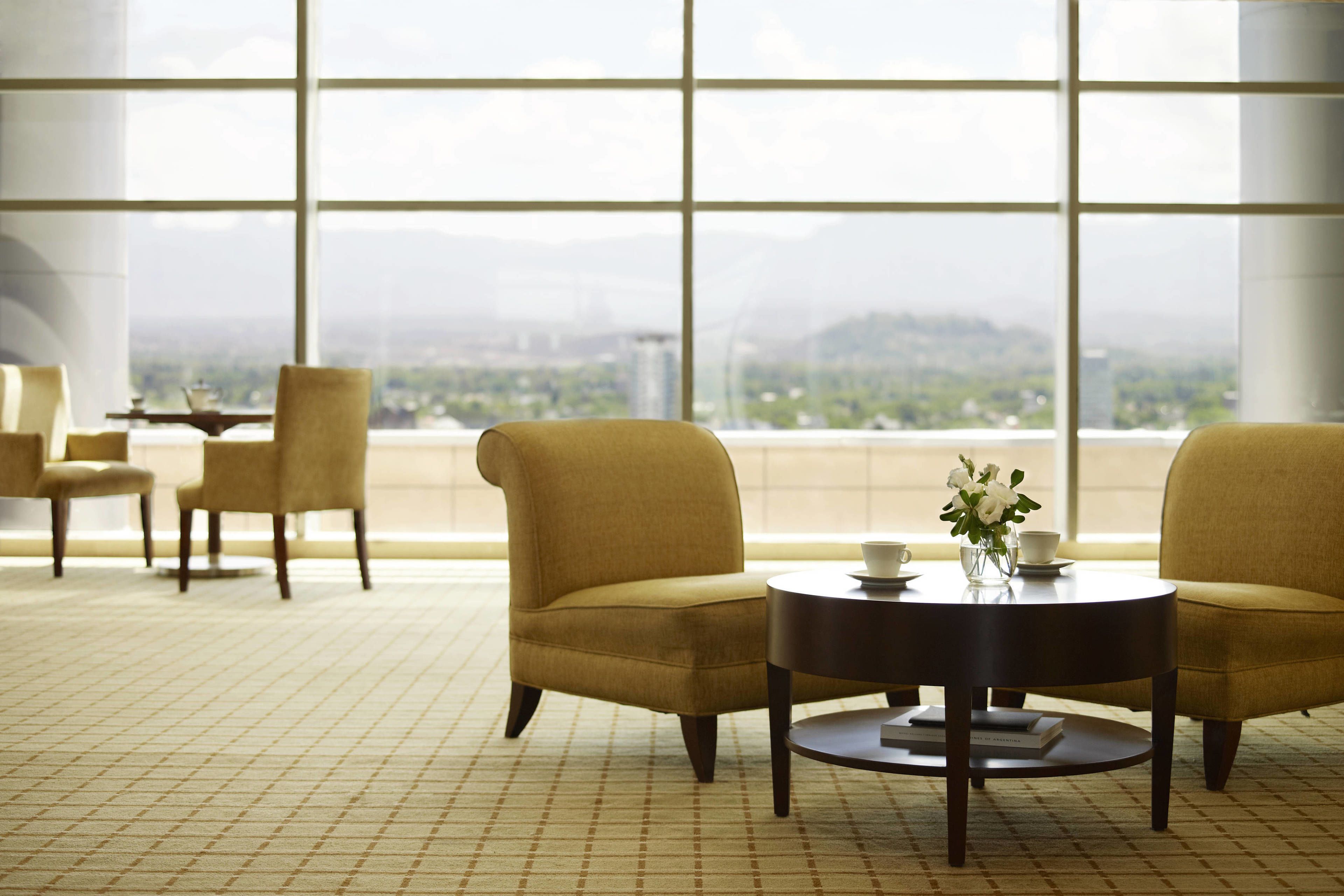 A spacious room with large windows, a round table with a vase of flowers, and two armchairs.