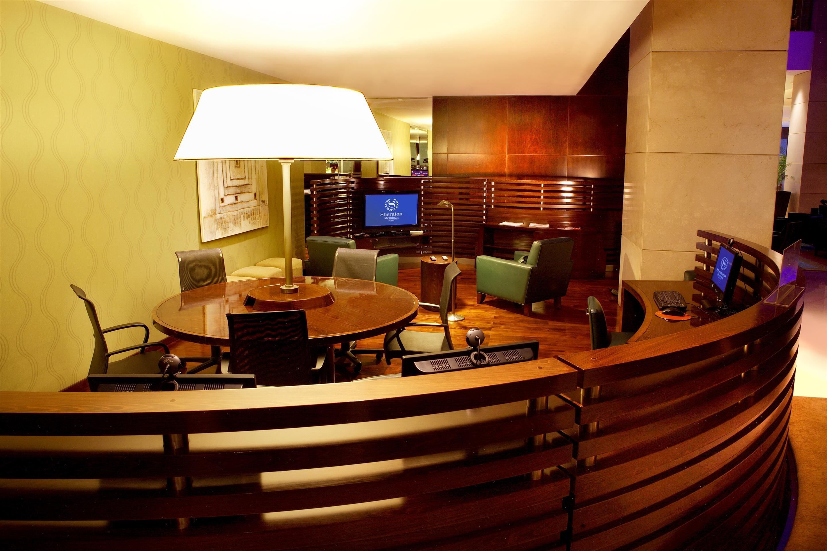 A hotel lobby with a round wooden table, several chairs, a television, and a reception desk.