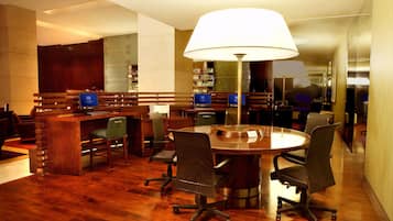 Uma sala de conferências com uma mesa redonda, quatro cadeiras, uma escrivaninha e um abajur grande.