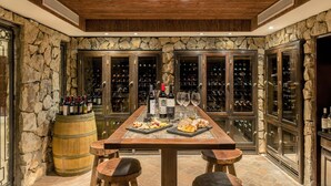 Una habitación de paredes de piedra con una mesa de madera dispuesta para una comida, botellas de vino y copas.