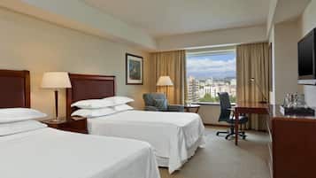 A hotel room with two beds, a desk, a chair, a TV, and a window with a city view.