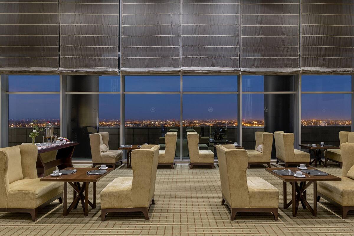 Un salon spacieux doté de plusieurs coins salon, de grandes fenêtres offrant une vue sur la ville et d’un aménagement intérieur moderne.