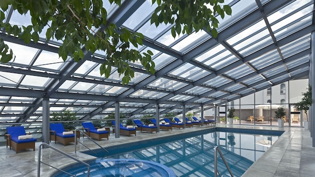 Una piscina interior con sillas reclinables azules y techo de cristal.