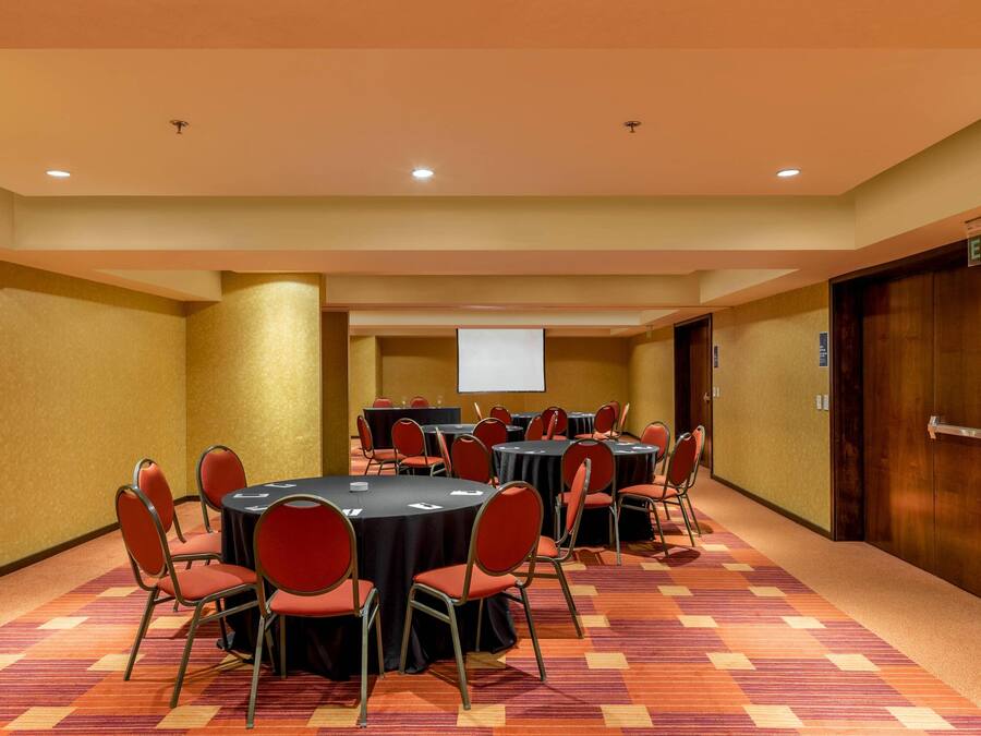 Sala de conferência com várias mesas e cadeiras, uma tela de projetor e uma porta de saída.