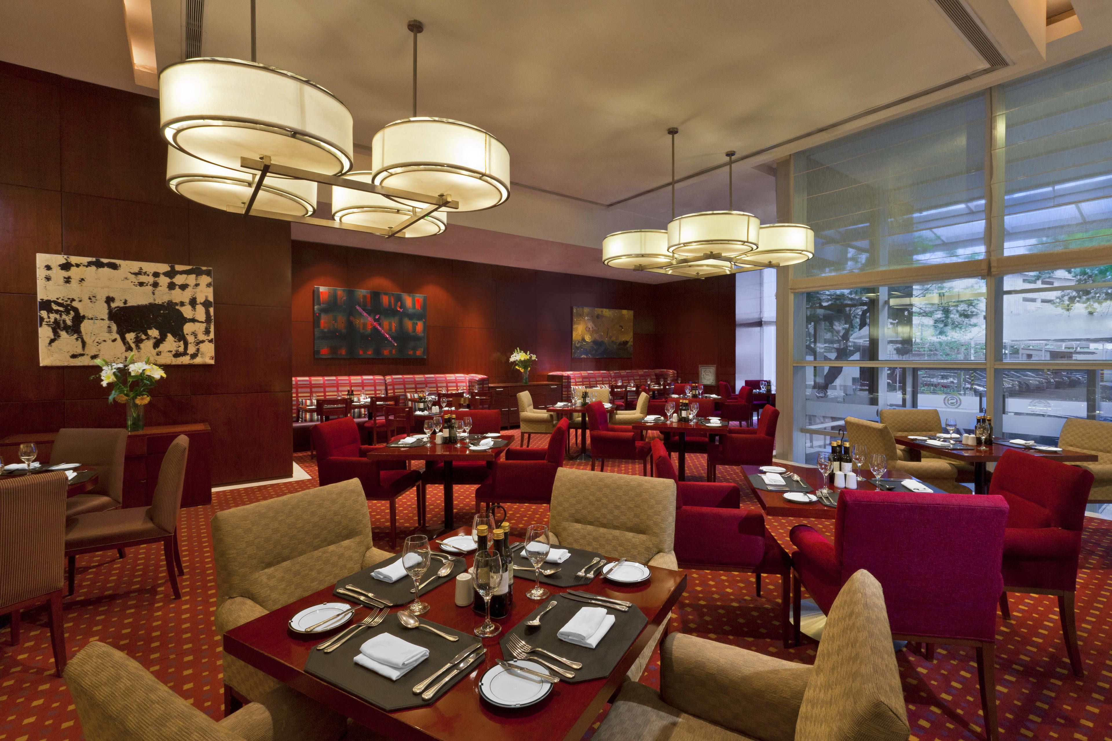 A restaurant with multiple dining tables, red chairs, and hanging light fixtures.