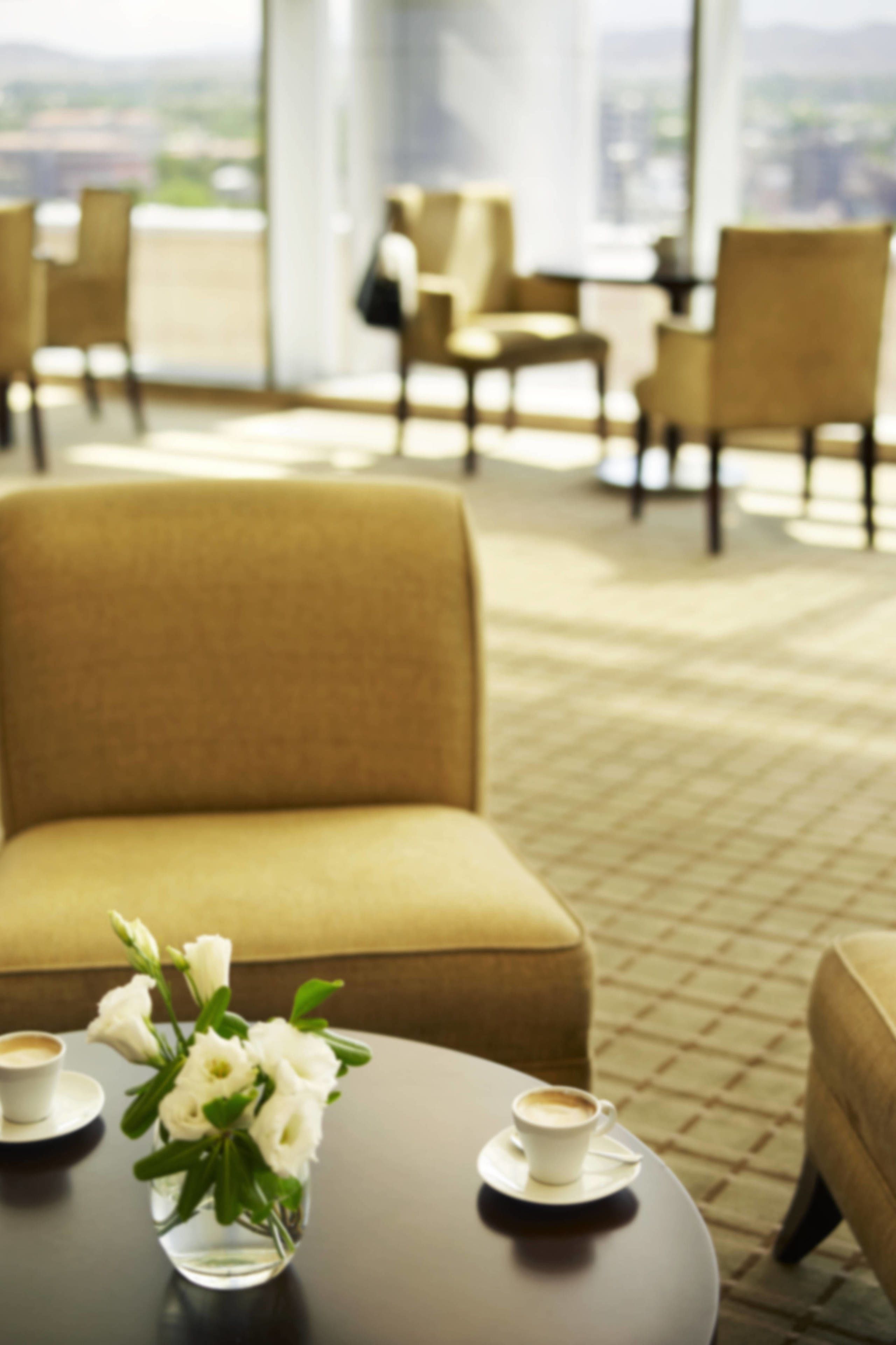 Un hall d’hôtel moderne, doté de sièges confortables, d’une table basse ornée d’un vase de fleurs et offrant une vue sur la ville.
