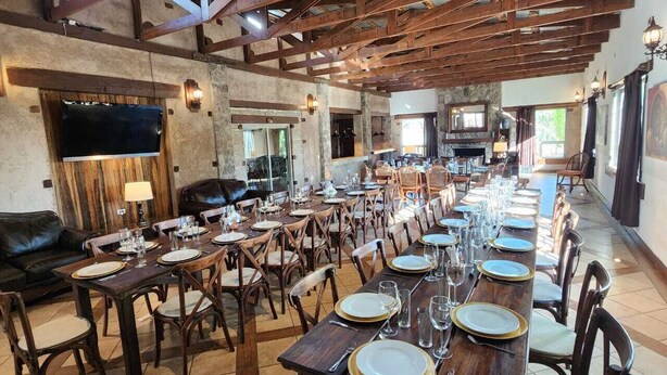 A spacious dining area with long wooden tables set for a meal, surrounded by stone walls and wooden beams. - Hotel Quinta Mision (Bocoyna)