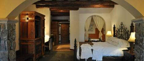 A bedroom with a stone fireplace, a bed with white linens, and a wooden wardrobe.
