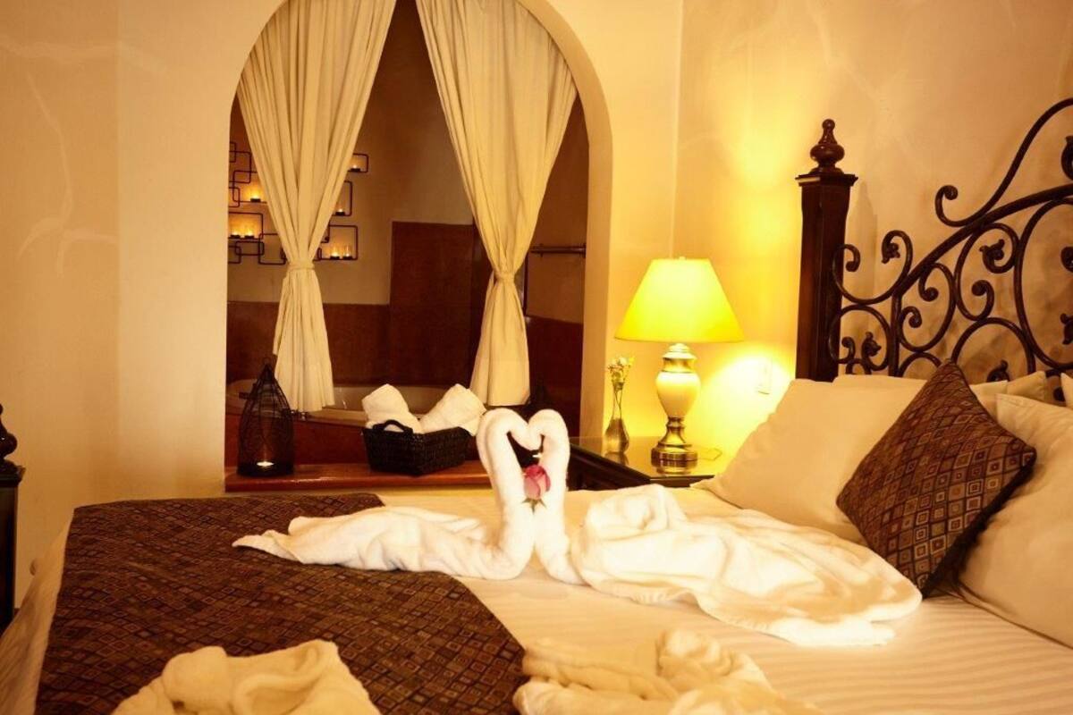 A hotel room with a bed, a nightstand with a lamp, a mirror, and a decorative wall.