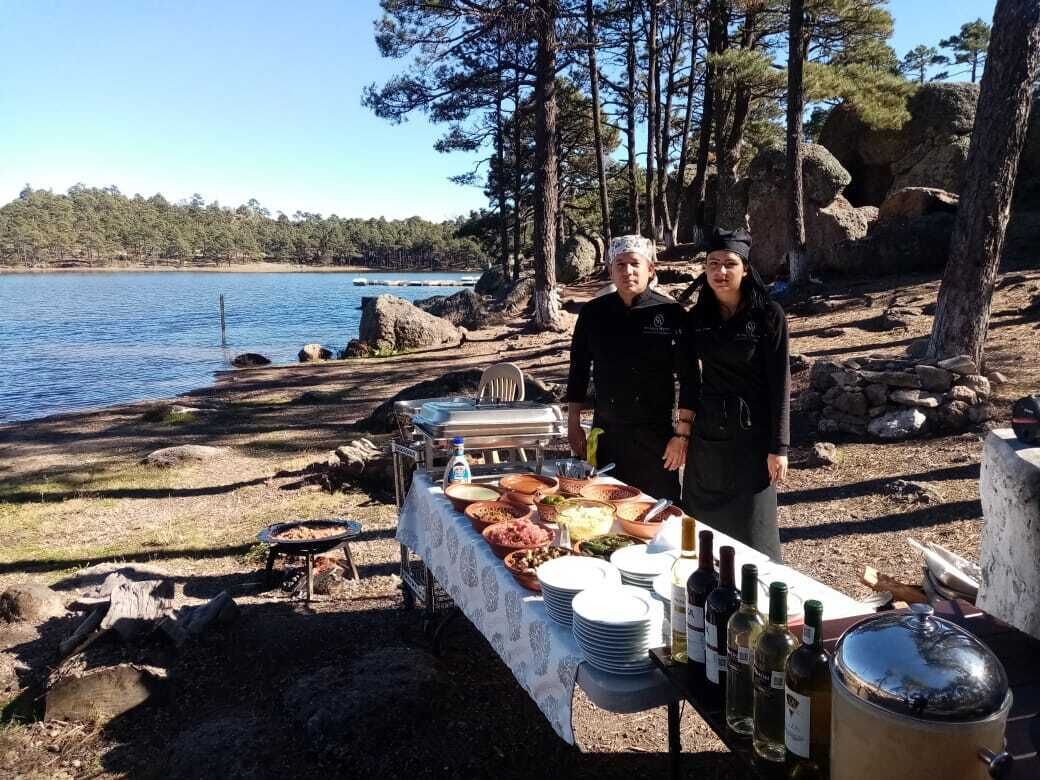 An outdoor dining setup with a table set for a meal, surrounded by natural scenery and a body of water.