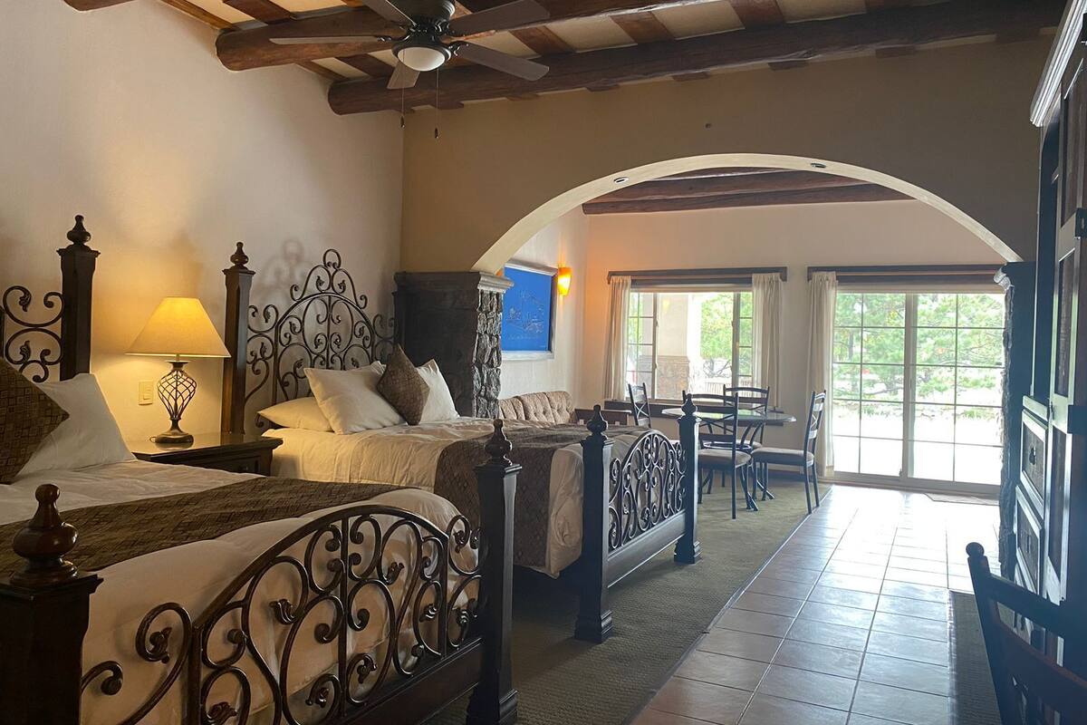 A bedroom with two beds, a sitting area with a table and chairs, and a view of the outdoors.