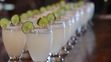 A row of glasses with lime garnishes on a bar counter, with small bowls of nuts in the foreground.