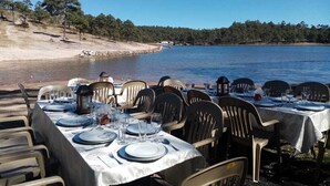 A dining table set up with chairs facing a lake, with a clear view of the water and trees in the background. - Hotel Quinta Mision (Bocoyna)