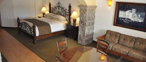 Un dormitorio con cama, mesitas de noche, un pilar de piedra, un sofá y una mesa con sillas.