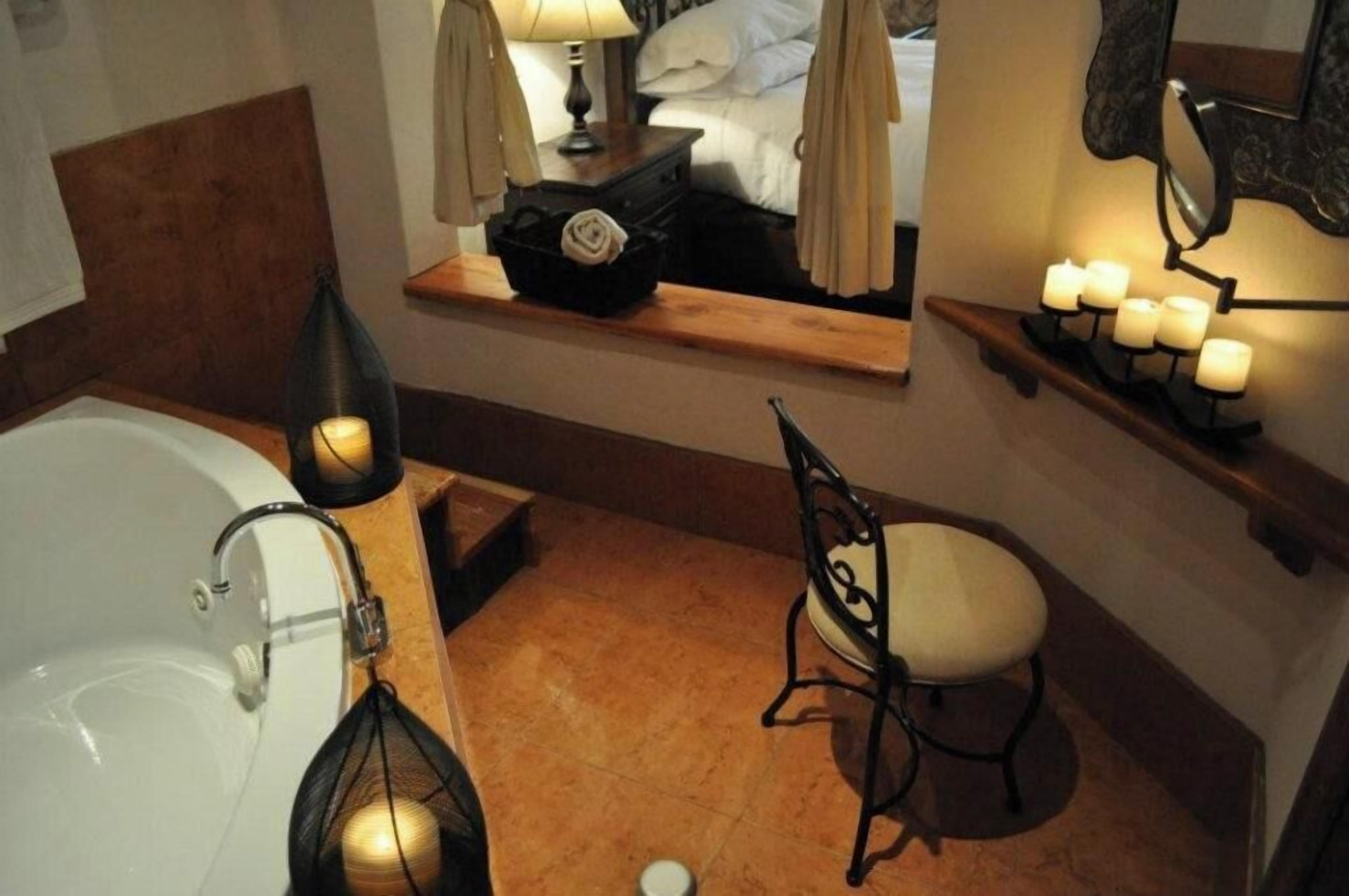 Casa de banho com banheira, pia, cadeira, espelho sobre a toucador e estante com velas.