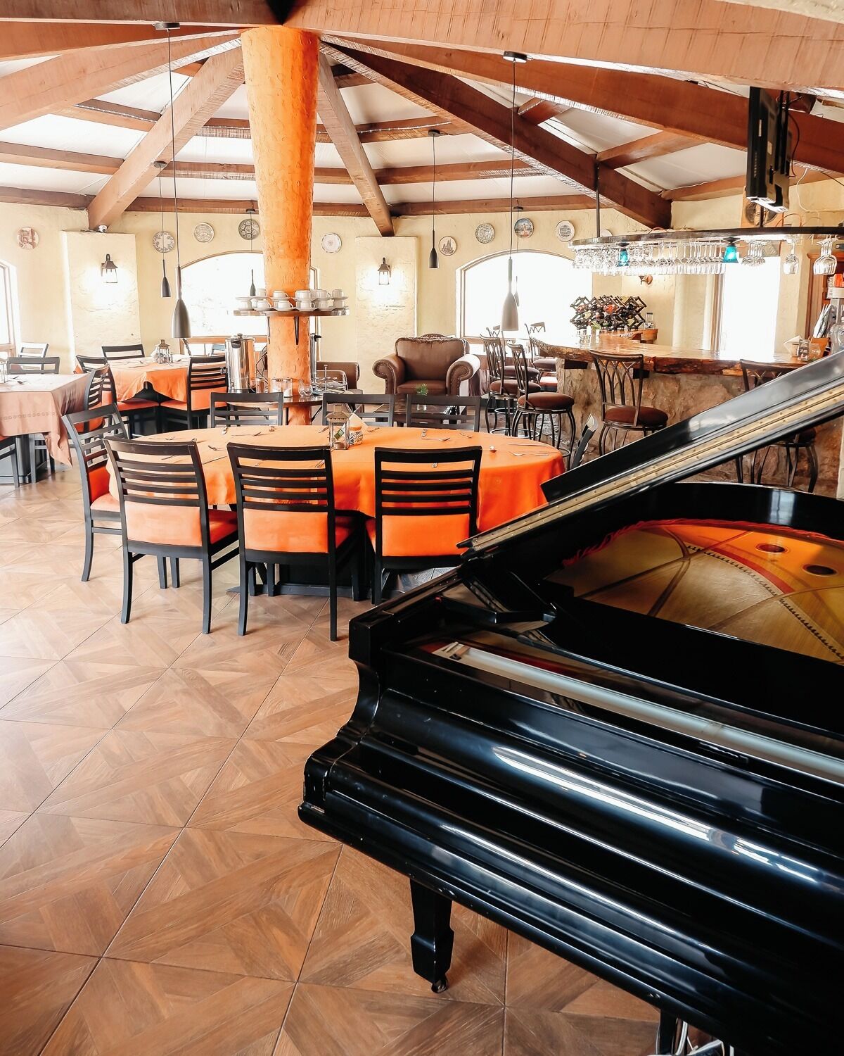 A dining area with tables and chairs, a grand piano, and a high ceiling with wooden beams.