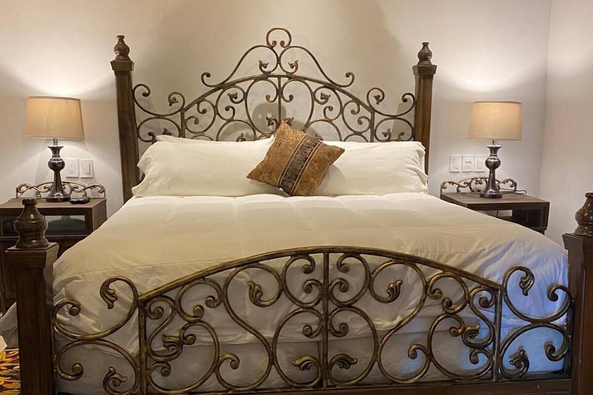 A four-poster bed with a decorative headboard, two bedside tables with lamps, and a richly patterned carpet.