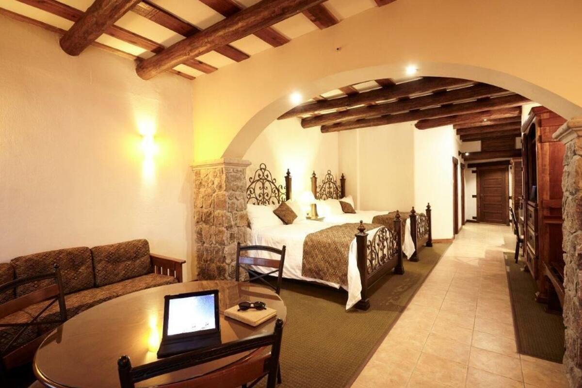 A cozy hotel room with a bed, a sitting area with a table and chairs, and a stone wall.