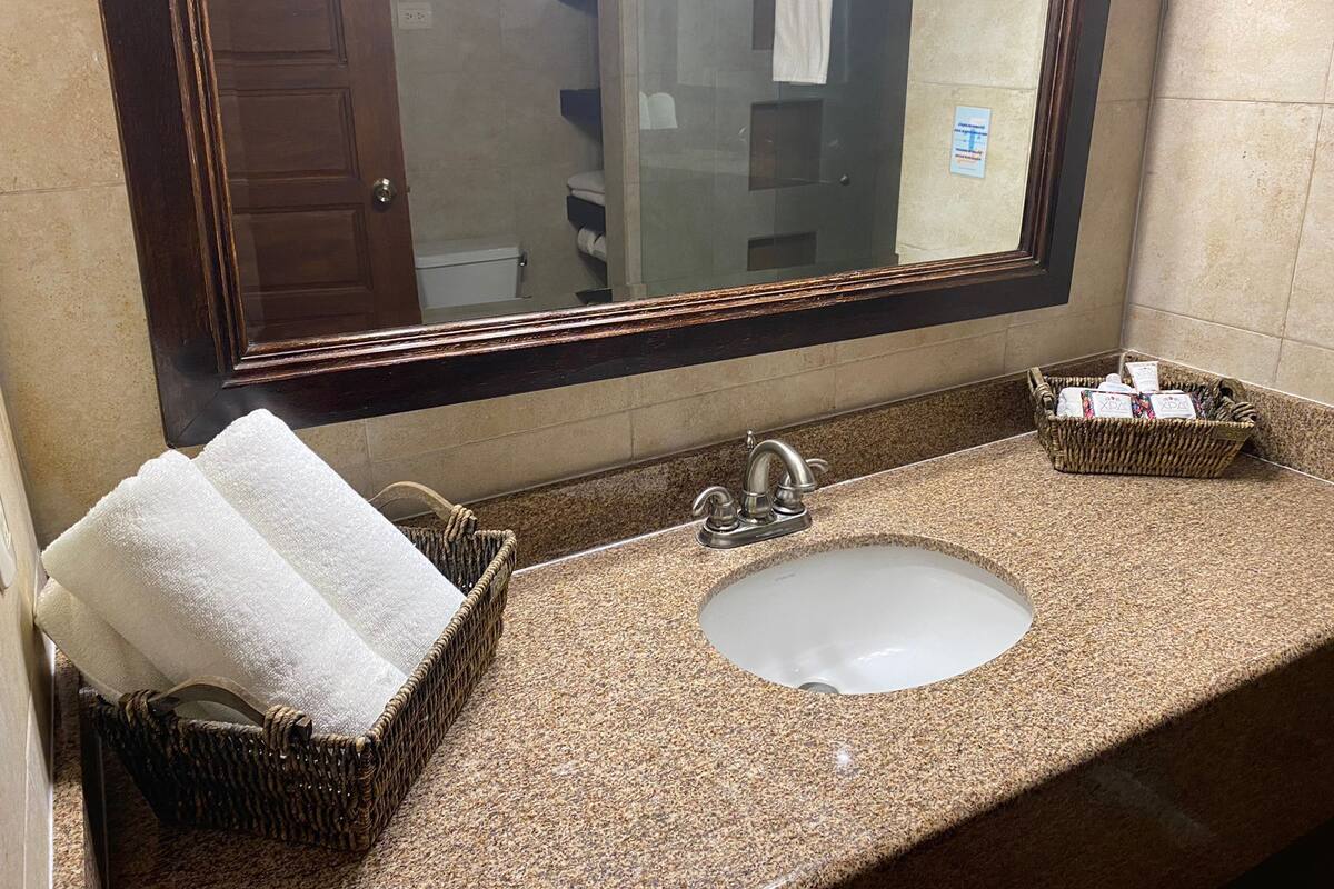 A bathroom with a granite countertop, a sink, a mirror, and two wicker baskets with towels.