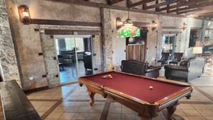 A pool table in a room with stone walls, wooden beams, and a hanging light fixture. - Hotel Quinta Mision (Bocoyna)