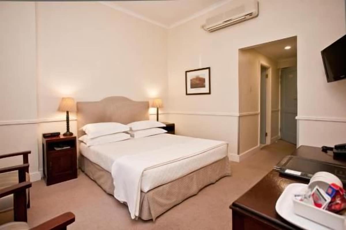 Una habitación de hotel con cama, lámparas de noche, escritorio, silla y televisión.