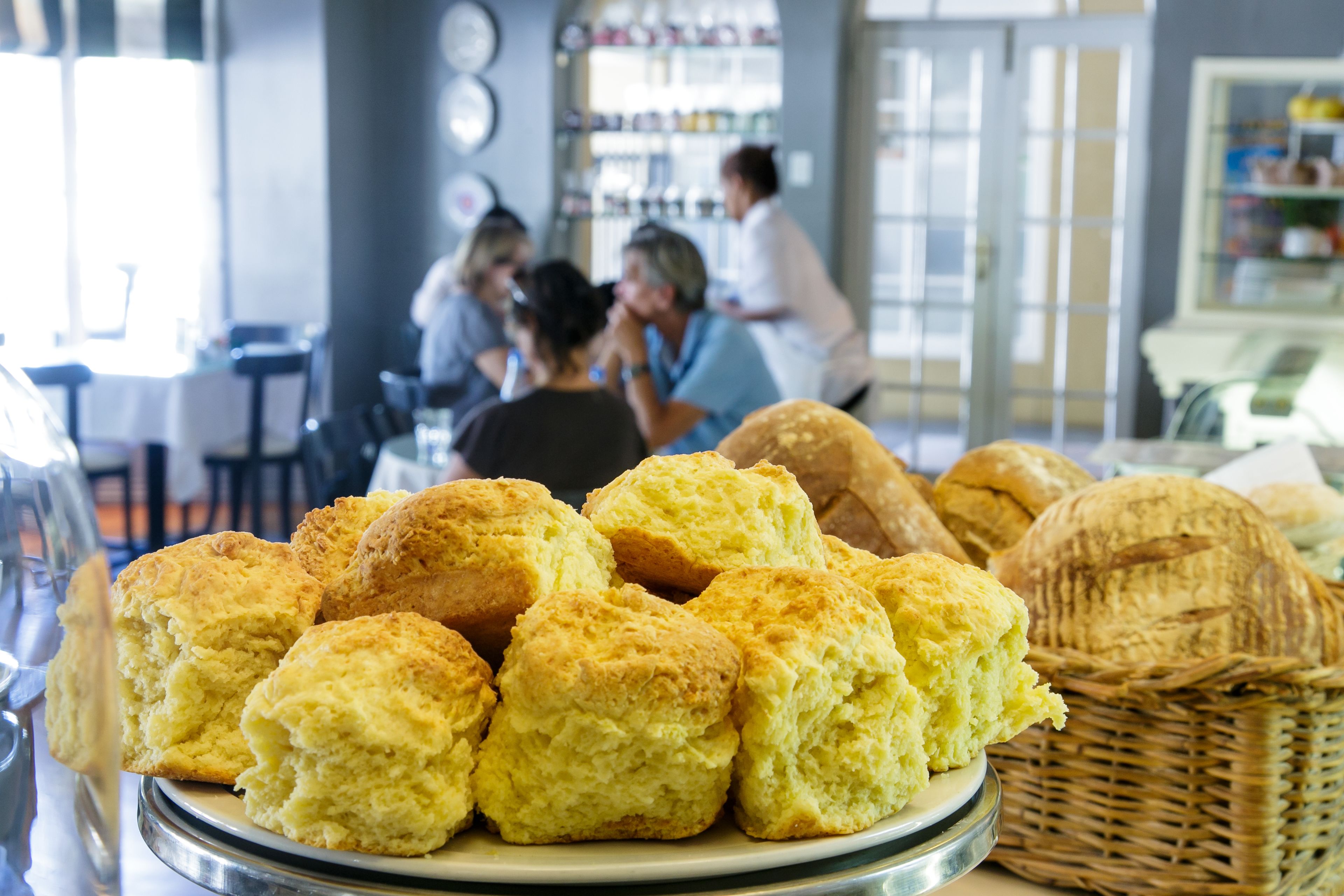 A plate of freshly baked biscuits and a basket of bread on a table in a cafe setting.