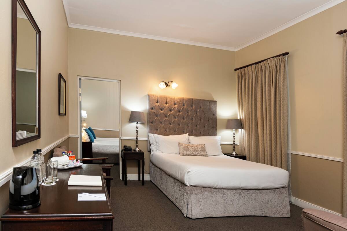 A hotel room with a large bed, bedside lamps, a desk with a kettle, and a mirror.