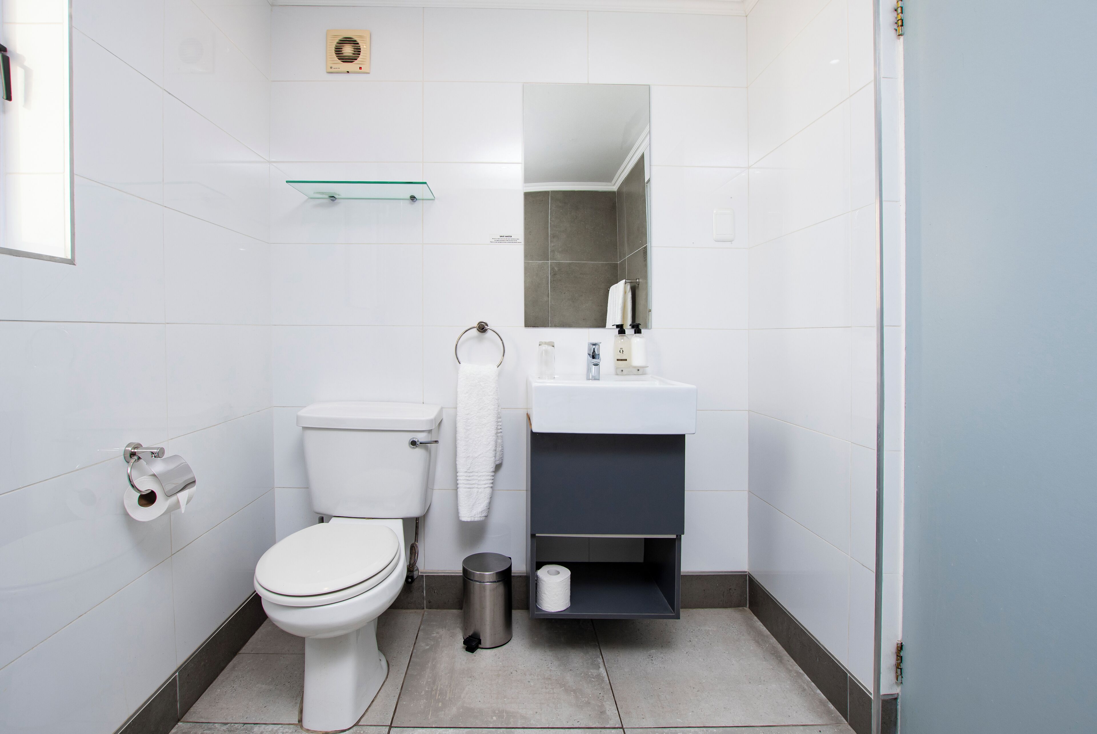 A modern bathroom with a toilet, sink, mirror, and glass shelf.