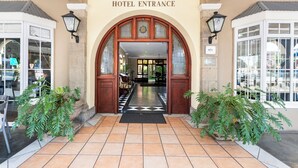 Entrada de hotel con suelo de baldosas, arco de madera y dos macetas.