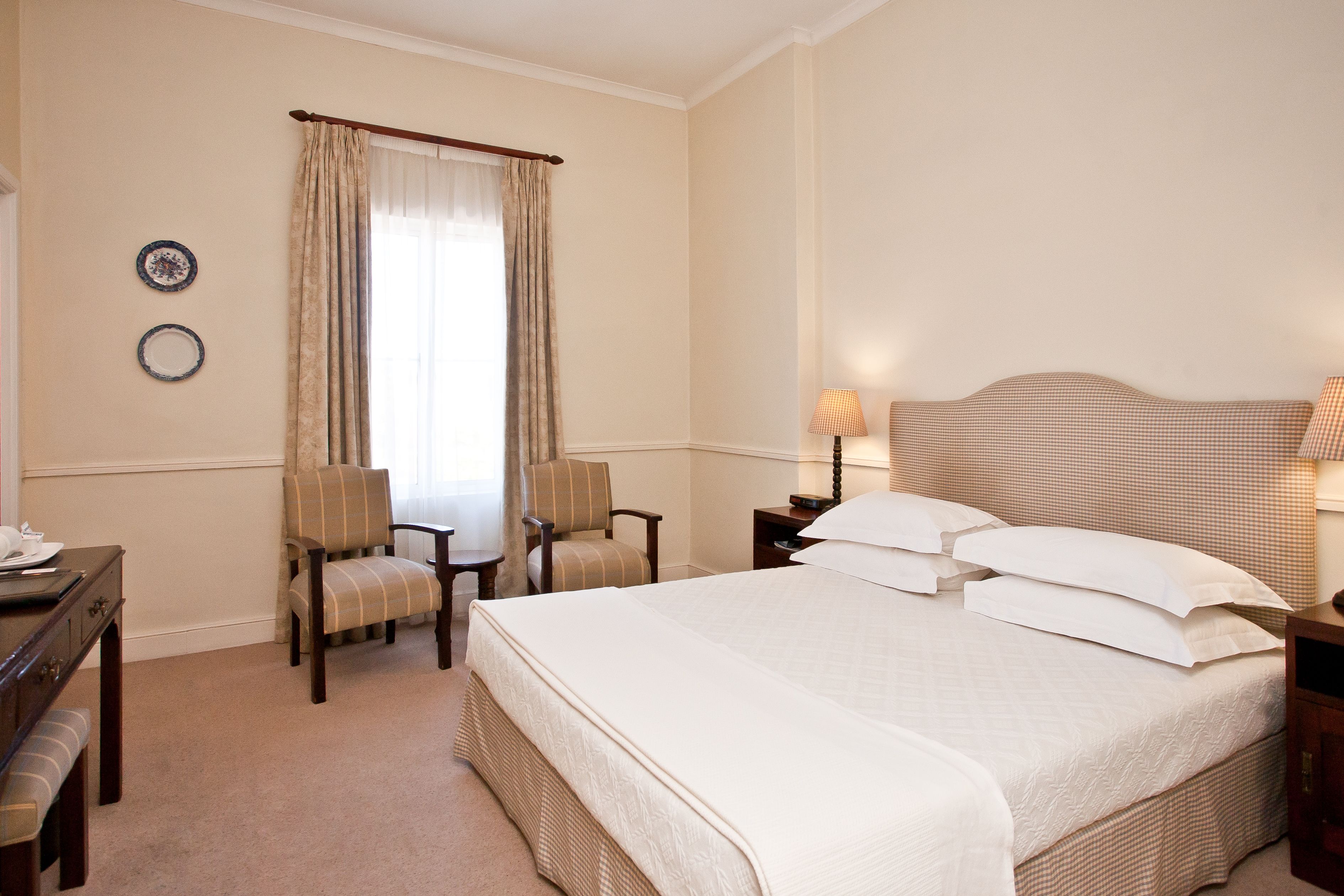 A hotel room with a large bed, two chairs, a desk, and a lamp.