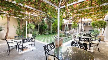 Un patio al aire libre con mesas y sillas, rodeado de follaje y un pequeño jardín.