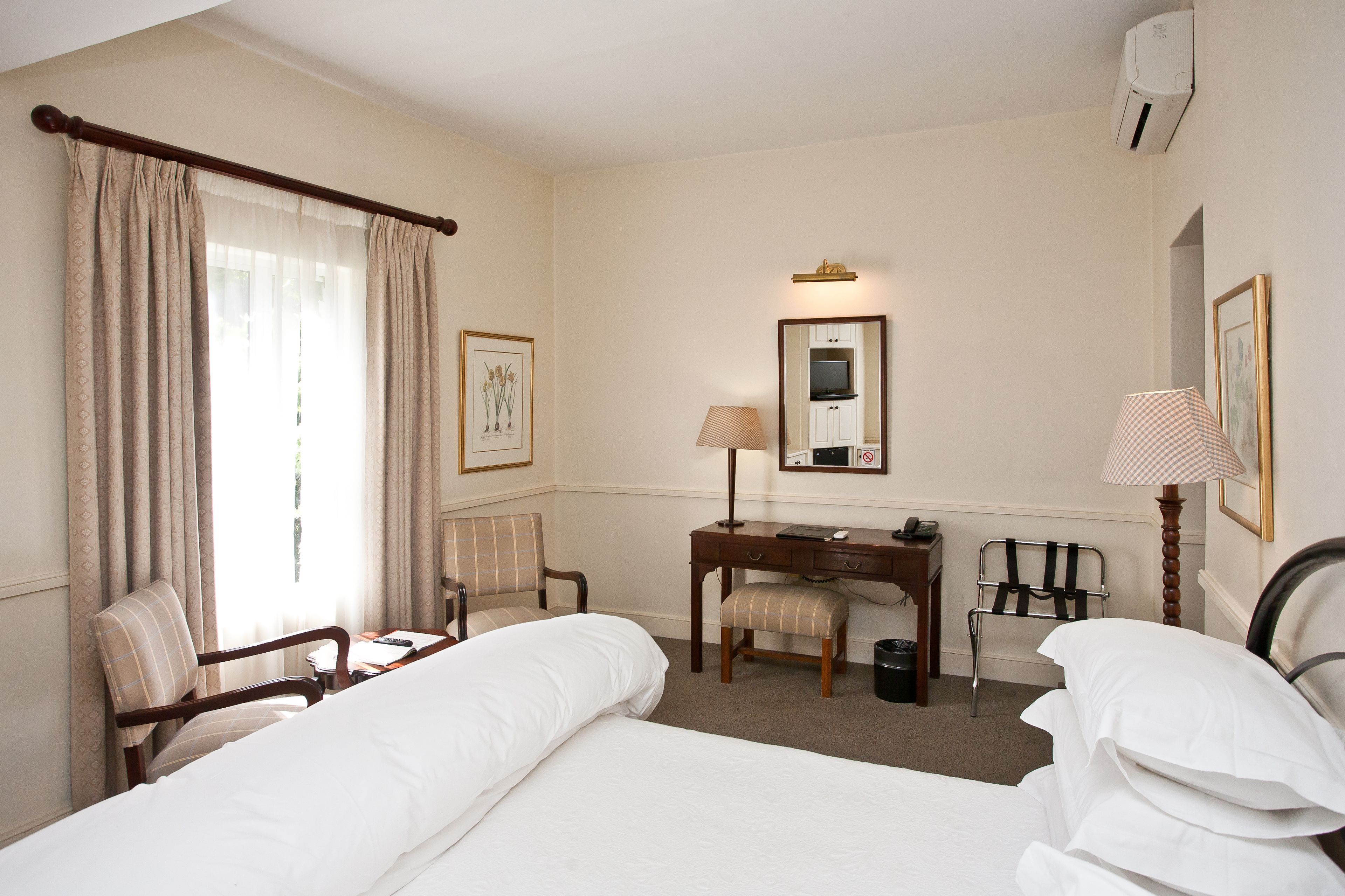 Une chambre d’hôtel avec deux lits, un bureau, une chaise, une lampe et un miroir.