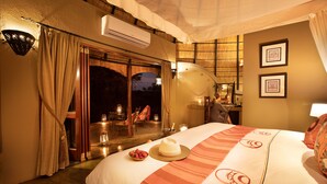 A hotel room with a bed, a dining area with a table and chairs, and a view of the outside. - Hoyo Hoyo Safari Lodge (Bushbuckridge)