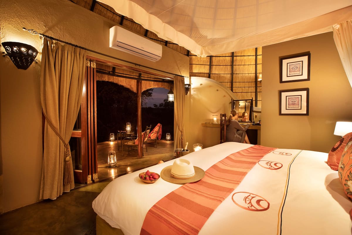 A hotel room with a bed, a dining area with a table and chairs, and a view of the outside.