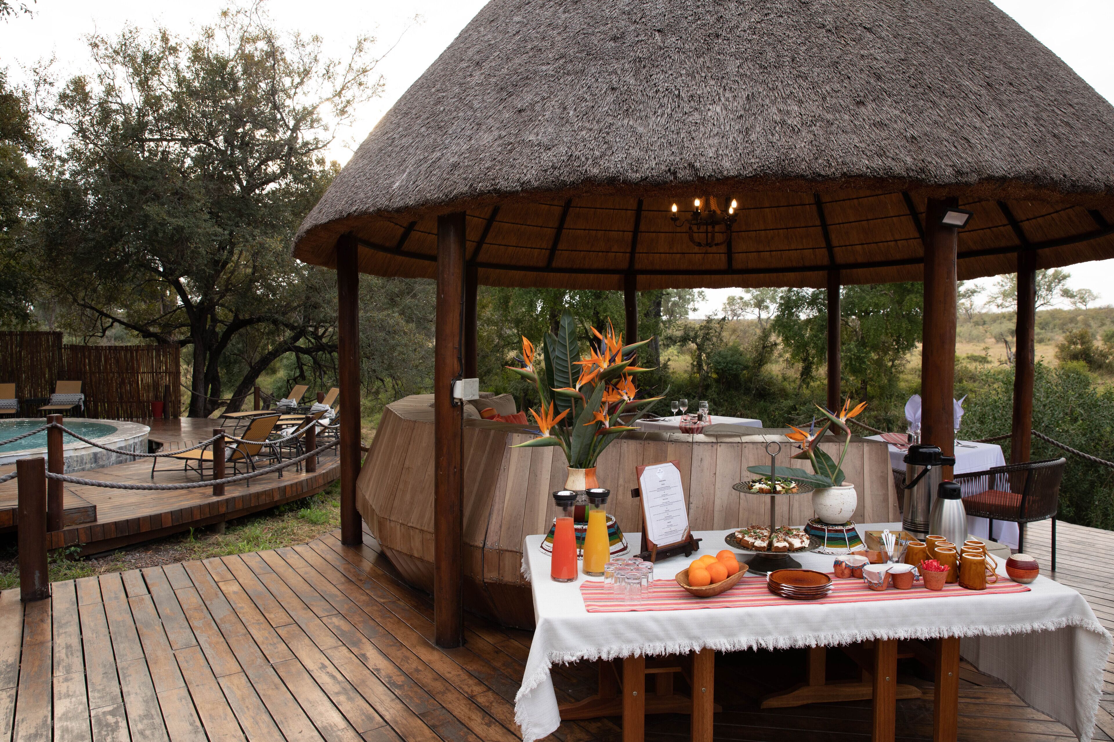 An outdoor dining area with a thatched roof, wooden deck, and a pool.