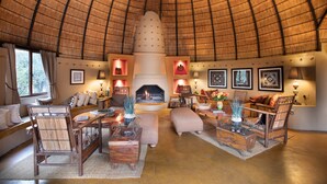 A cozy, circular room with a thatched roof, a fireplace, comfortable seating, and framed artwork on the walls. - Hoyo Hoyo Safari Lodge (Bushbuckridge)