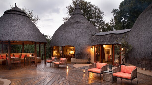 A thatched-roof structure with a wooden deck, outdoor seating, and a stone wall. - Hoyo Hoyo Safari Lodge (Bushbuckridge)