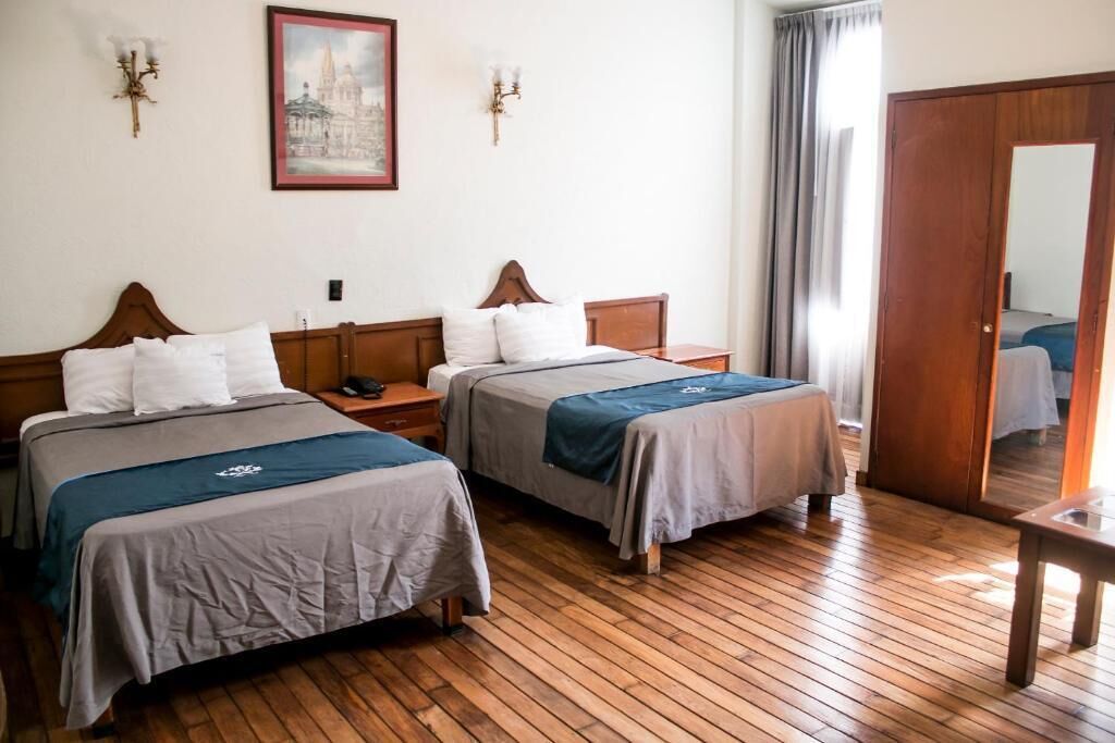 A hotel room with two beds, wooden flooring, a wooden wardrobe, and a painting on the wall.