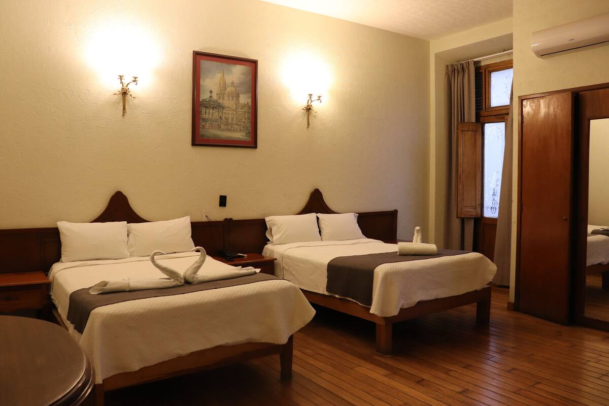 A hotel room with two beds, a painting on the wall, and a mirror reflecting part of the room.
