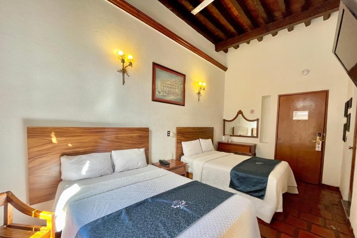 A hotel room with two beds, a wooden headboard, a wooden chair, a wooden door, and a wall-mounted light fixture.