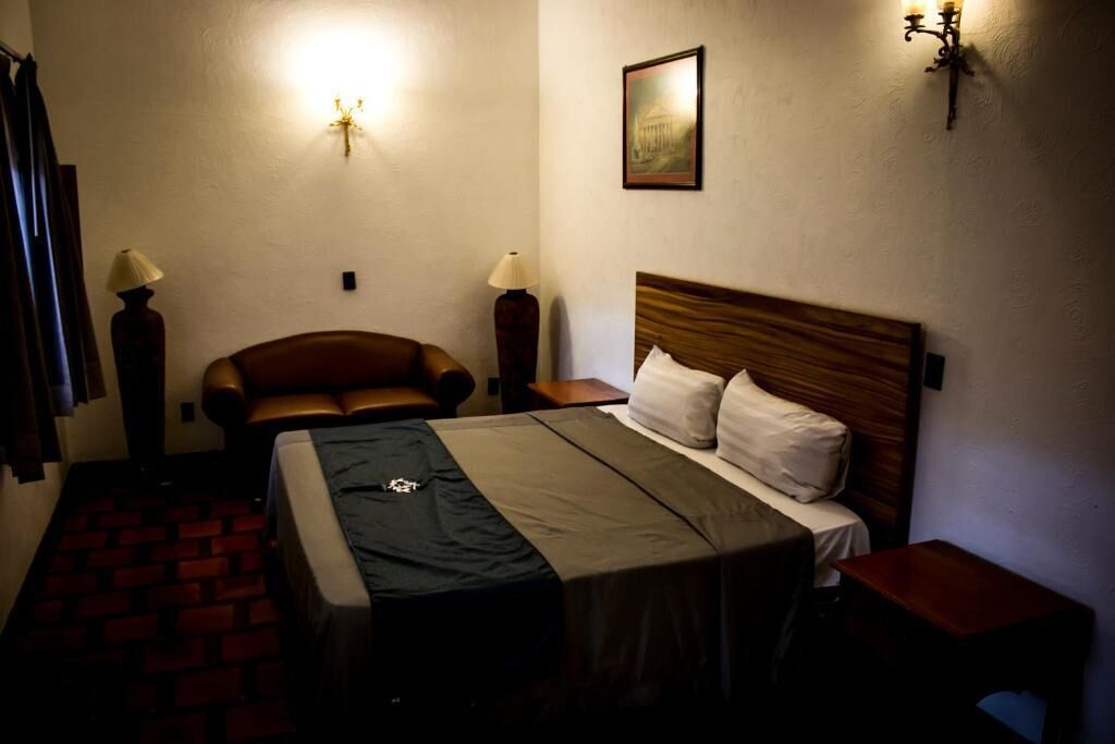 Een hotelkamer met een bed, een stoel, een klein tafeltje en een lamp.