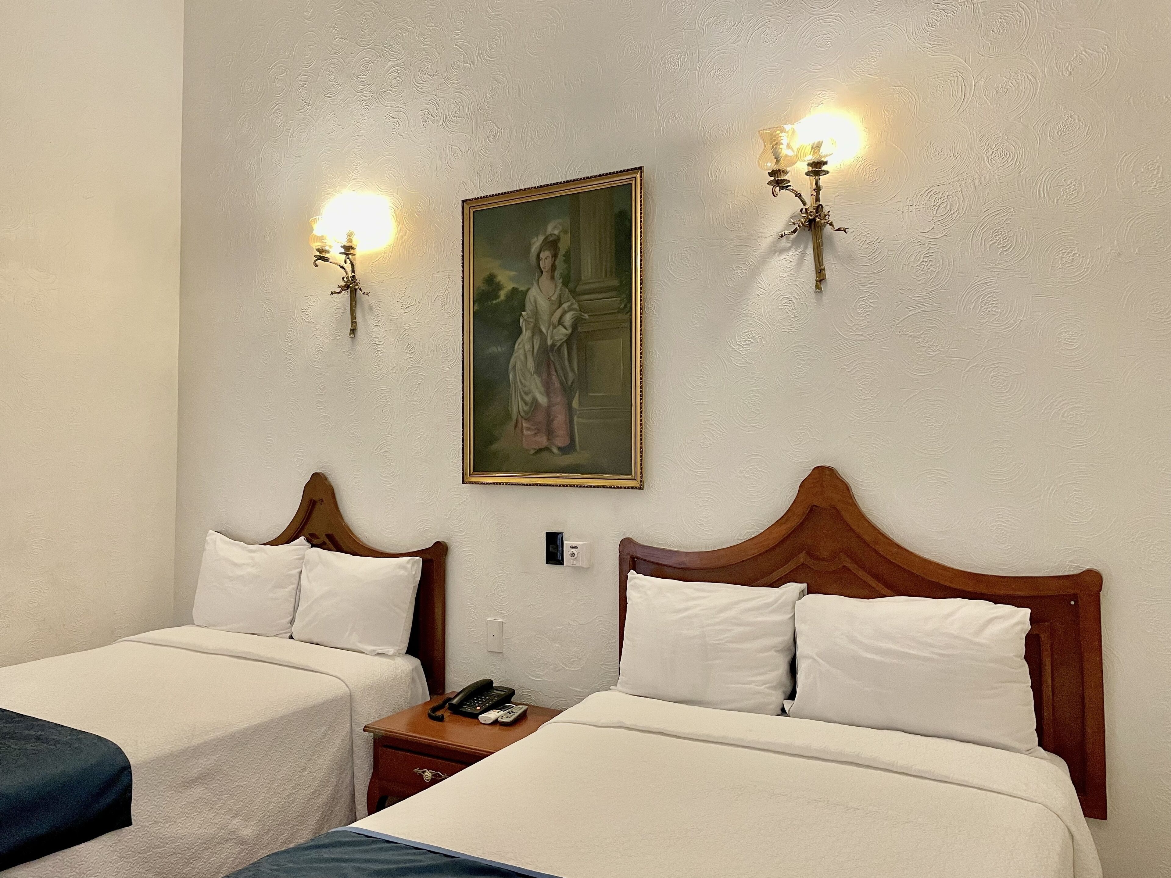 Una habitación de hotel con dos camas, un cuadro en la pared y dos lámparas de pared.