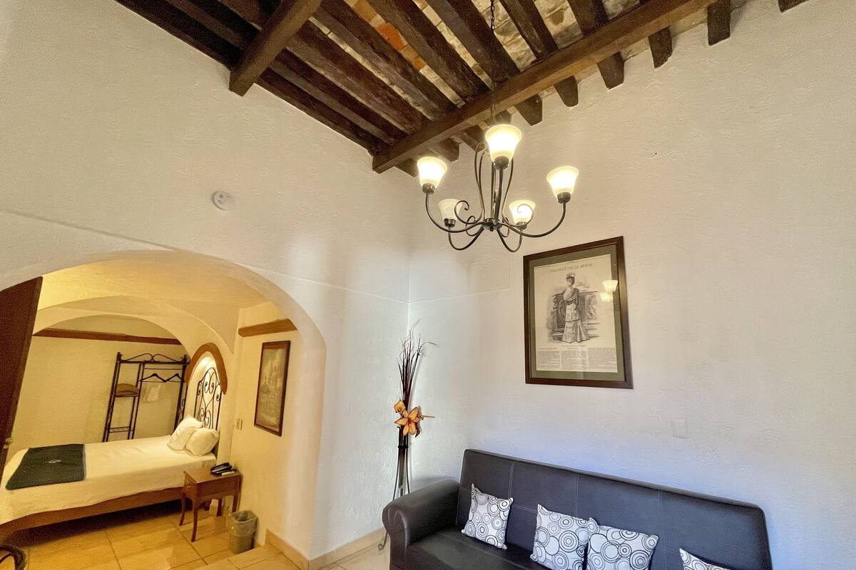 A room with a bed, a black sofa, a chandelier, and a framed picture on the wall.