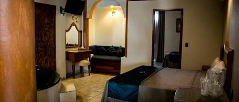 Habitación de hotel compacta con cama, escritorio, silla, mesita, espejo y televisor.