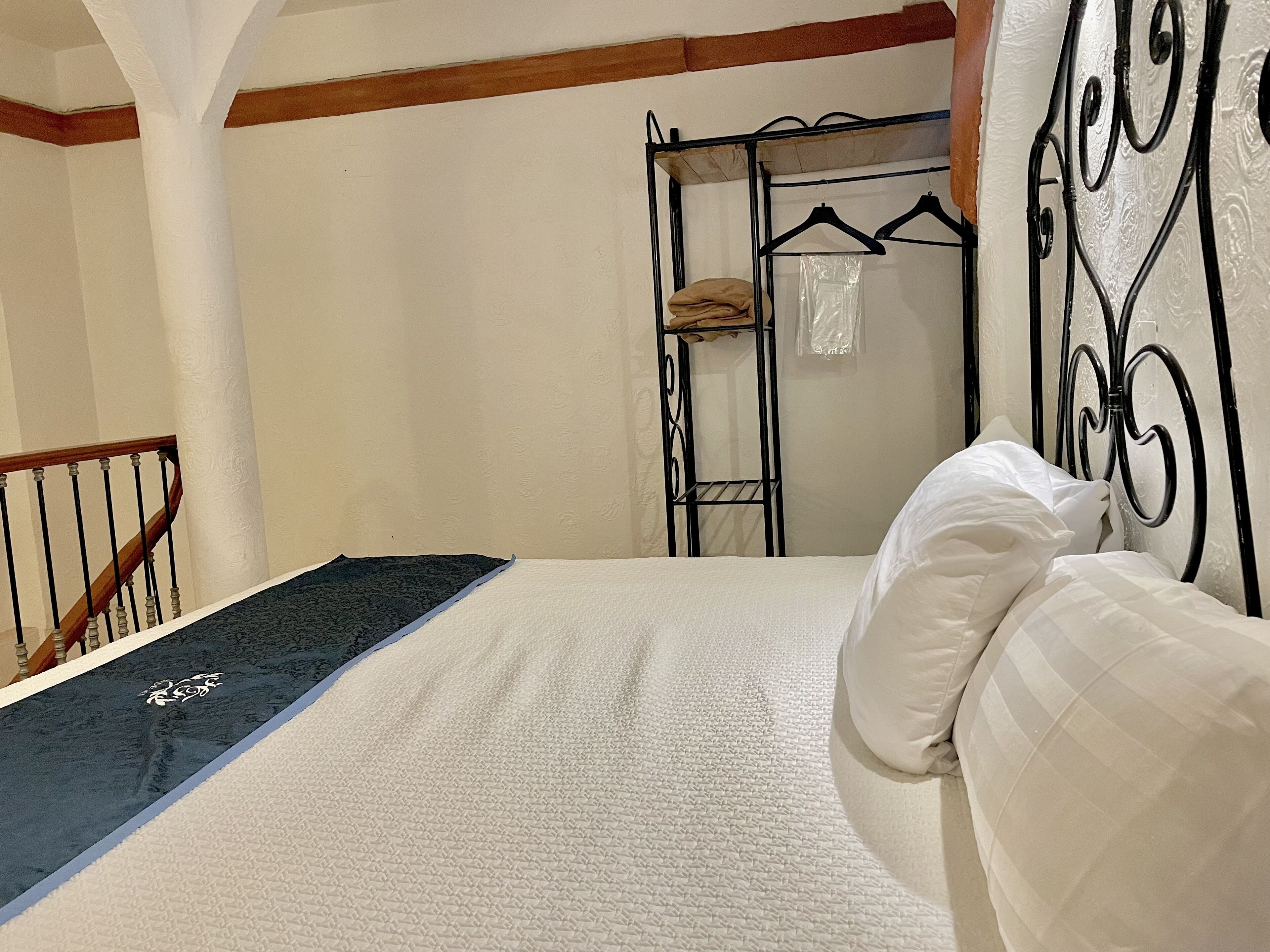 Un dormitorio con cama, armario metálico y escalera.