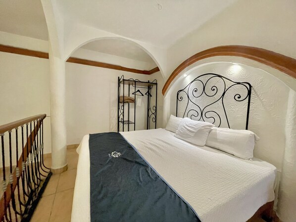 A bedroom with a bed, a metal headboard, a wooden railing, and a white wall with a wooden beam.