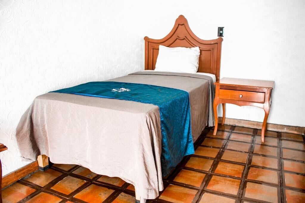 Un lit simple avec une tête de lit en bois, une table de chevet avec un tiroir et un sol carrelé.