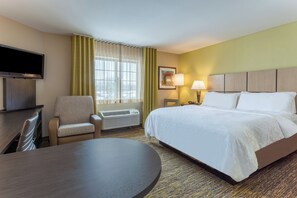 Habitación de hotel con cama, escritorio, silla, televisor, ventana con cortinas, lámpara y un cuadro en la pared.