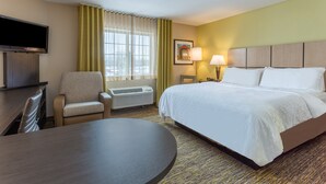 Ein Hotelzimmer mit Bett, Schreibtisch, Stuhl, Fernseher, Lampe und einem Fenster mit Vorhängen.