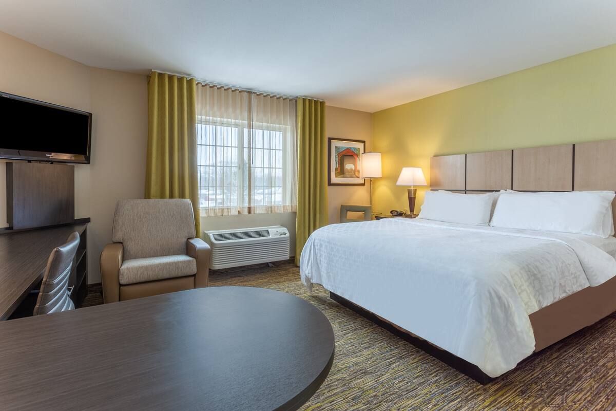 Une chambre d’hôtel équipée d’un lit, d’un bureau, d’une chaise, d’une télévision, d’une lampe et d’une fenêtre avec des rideaux.